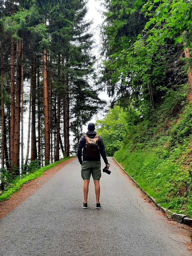 Sebastian von hinten auf einem Waldweg, mit Kamera und Rucksack unterwegs